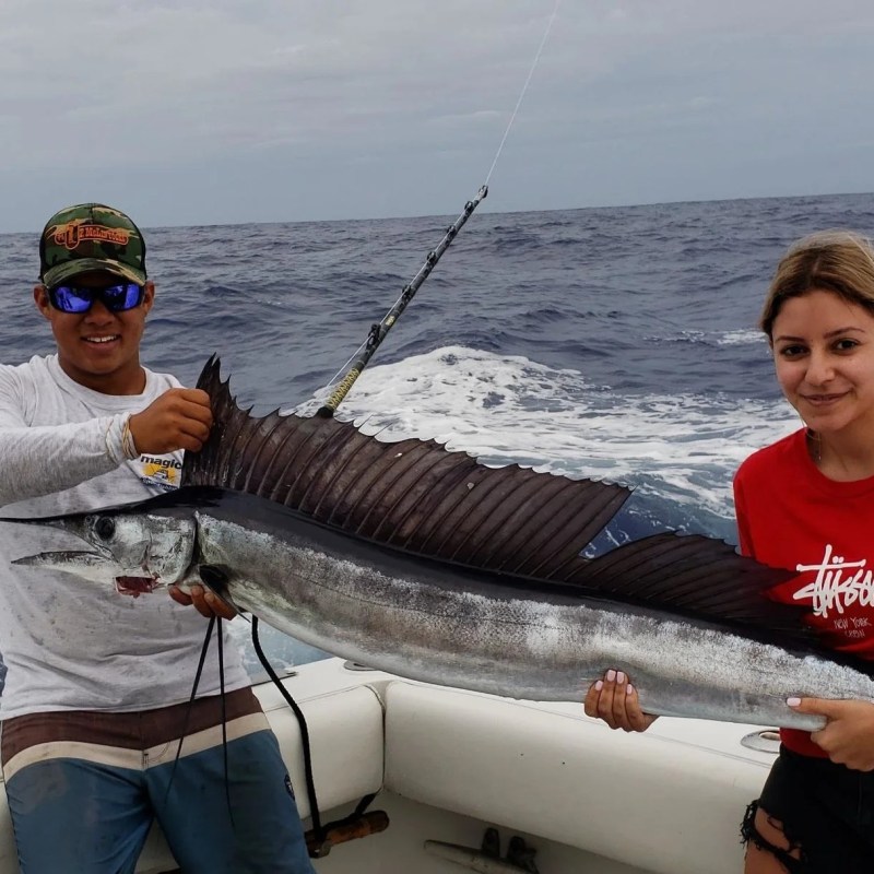 Two people on a boat holding a large fish over the ocean.